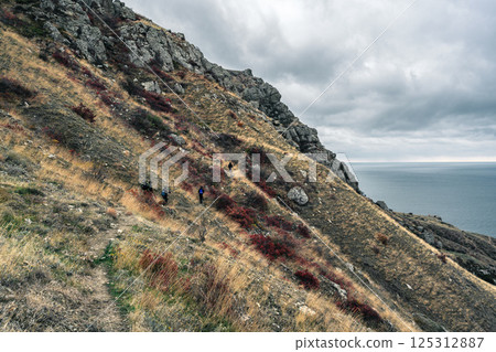 Hiking along a rugged coastal trail with dramatic cliffs and ocean views on a cloudy day Hiking along a rugged coastal trail with dramatic cliffs and ocean views on a cloudy day 125312887