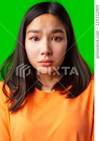 Young woman with long dark hair expresses surprise against a bright green background 125312905