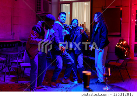 Friends enjoying a lively celebration at a vibrant outdoor gathering at night in a cozy courtyard 125312913