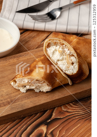 Delicious rolled pancakes filled with creamy cheese on a wooden board Delicious rolled pancakes filled with creamy cheese on a wooden board 125312959