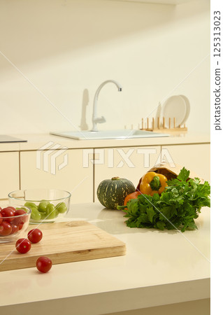 Few cherry tomatoes are scattered on a wooden cutting board, and berries and green grapes are placed in a glass bowl. Vegetables in a paper bag on marble table. Modern kitchen with full equipment. Few cherry tomatoes are scattered on a wooden cutting board, and berries and green grapes are placed in a glass bowl. Vegetables in a paper bag on marble table. Modern kitchen with full equipment. 125313023