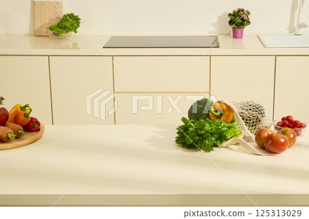 Glass bowl of cherry potatoes placed behind some fresh tomatoes. Celery, cauliflower and bell peppers are placed in beige mesh bags, arranged on a stone dining table. Modern kitchen background. Glass bowl of cherry potatoes placed behind some fresh tomatoes. Celery, cauliflower and bell peppers are placed in beige mesh bags, arranged on a stone dining table. Modern kitchen background. 125313029
