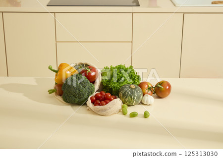 Lettuce, broccoli, bell peppers, carrots, pumpkin, tomatoes, garlic, and a mesh bag of cherry tomatoes cluster on a table. Green grapes line the other vegetables. Fresh organic food in the kitchen. 125313030