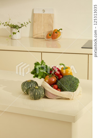 Vertical photo of fresh vegetables in mesh bag, including cauliflower, tomatoes, bell peppers, celery, etc. Potted plants next to wooden cutting board, displayed on kitchen counter for decoration. Vertical photo of fresh vegetables in mesh bag, including cauliflower, tomatoes, bell peppers, celery, etc. Potted plants next to wooden cutting board, displayed on kitchen counter for decoration. 125313035