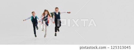 Banner. children in uniform jumping forward hand in hand with backpacks and excited faces. Copy space. Concept of back to school 125313045