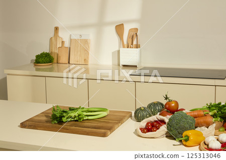 Modern kitchen fully equipped with cooking appliances such as induction cooker, wooden cutting board. Fresh vegetables are placed on the kitchen counter. Celery is ready for processing. Modern kitchen fully equipped with cooking appliances such as induction cooker, wooden cutting board. Fresh vegetables are placed on the kitchen counter. Celery is ready for processing. 125313046