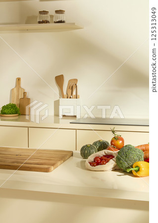Photo of a cozy kitchen corner. The wooden shelves above hold jars of cereal. The induction cooker is flush mounted to the counter. Vegetables and fruits are arranged in a natural way. Copy space. 125313049