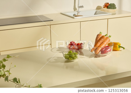 Top view of fresh vegetables such as carrots, tomatoes, bell peppers and green grapes, placed in clear glass bowls. Electric stove and sink are used for cooking. Modern Kitchen in warmly home Top view of fresh vegetables such as carrots, tomatoes, bell peppers and green grapes, placed in clear glass bowls. Electric stove and sink are used for cooking. Modern Kitchen in warmly home 125313056