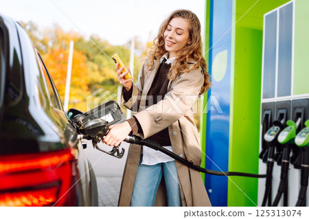 Young woman filling her car at the gas station. You can Online pay. Woman pays for a gas station Young woman filling her car at the gas station. You can Online pay. Woman pays for a gas station 125313074