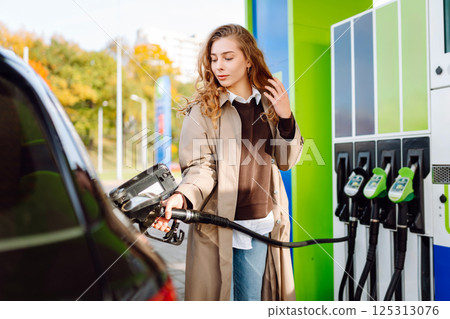 Young woman filling her car at the gas station. You can Online pay. Woman pays for a gas station 125313076