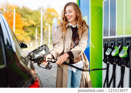 Young woman filling her car at the gas station. You can Online pay. Woman pays for a gas station Young woman filling her car at the gas station. You can Online pay. Woman pays for a gas station 125313077