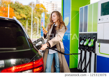 Young woman filling her car at the gas station. You can Online pay. Woman pays for a gas station 125313078