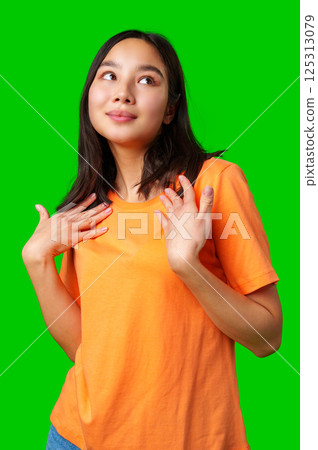 Young woman poses confidently in bright orange shirt against vibrant green background 125313079