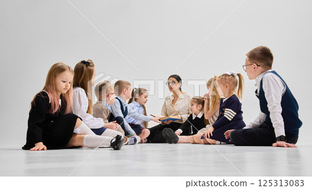Smiling students listening to storytime as teacher reads aloud from book in classroom circle. Concept of joy of reading Smiling students listening to storytime as teacher reads aloud from book in classroom circle. Concept of joy of reading 125313083