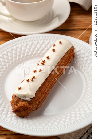 Delicious eclair topped with creamy frosting and golden sprinkles on a decorative plate 125313105
