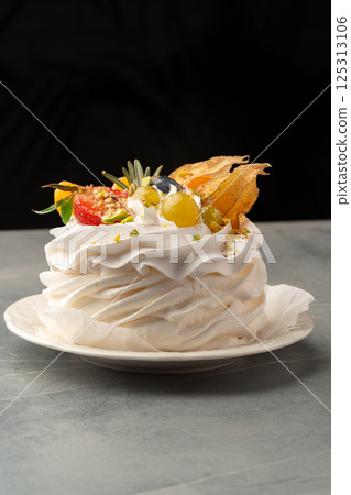 Delightful meringue dessert topped with fresh fruits and edible flowers on a simple plate Delightful meringue dessert topped with fresh fruits and edible flowers on a simple plate 125313106