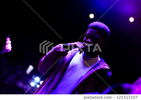 Young man posing under vibrant lighting at an urban music event during the nighttime 125313107