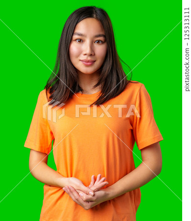 Young woman in an orange t-shirt poses confidently against a bright green backdrop indoors Young woman in an orange t-shirt poses confidently against a bright green backdrop indoors 125313111