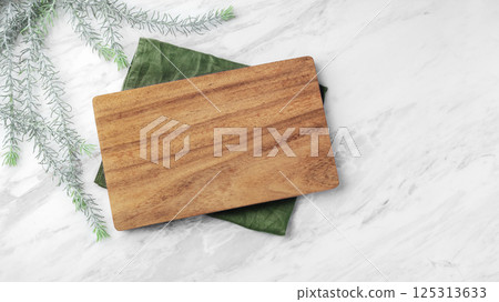 Wood plate board on green linen napkin on natural marble table, top view Wood plate board on green linen napkin on natural marble table, top view 125313633
