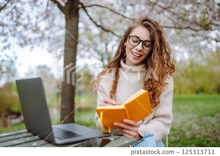Beautiful female student is using laptop, notepad to prepare for outdoor classes. Education concept. 125313711