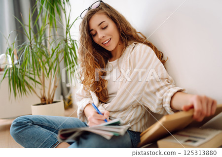 Happy woman sitting on floor in living room, enjoying reading book. Concept of relaxation, comfort. Happy woman sitting on floor in living room, enjoying reading book. Concept of relaxation, comfort. 125313880