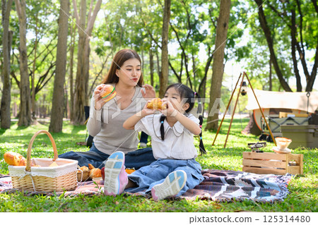 Mother and child having a delicious meal together while camping in a sunny wooded area 125314480