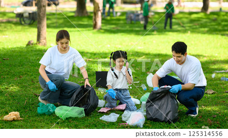 Parents and child picking up plastic waste together during a park cleanup activity 125314556