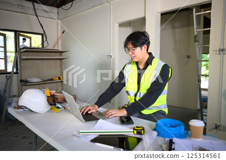 Engineer using laptop to review plans and manage site progress in a home renovation Engineer using laptop to review plans and manage site progress in a home renovation 125314561
