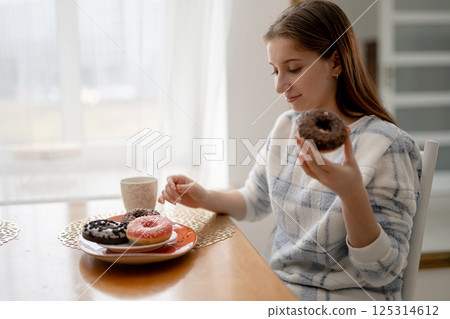 Young Girl In Pajamas Eating Donuts In The Kitchen 125314612