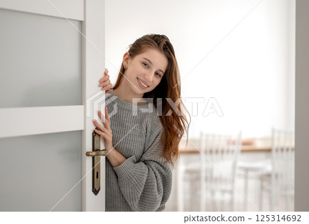 Young Cute Girl With Long Hair Peeks From Behind The Door And Smiles 125314692