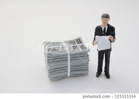 Businessman Reading a Document Beside a Stack of Newspapers 125315314