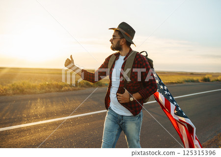 4th of July. American Flag. Traveler with the flag of America. The man in a hat, a backpack, a shirt and jeans. 4th of July. American Flag. Traveler with the flag of America. The man in a hat, a backpack, a shirt and jeans. 125315396