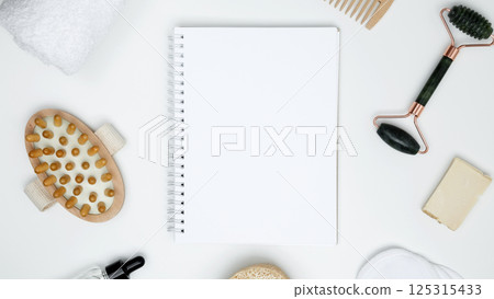 Mock up white notebook, sustainable self-care concept. Eco-friendly beauty products: massage brush, loofah, marble roller, towel, reusable cotton pads 125315433