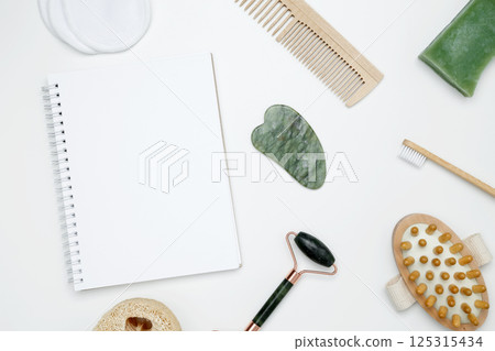Eco-friendly beauty products: massage brush, loofah, marble roller, towel, reusable cotton pads, mock up white notebook, sustainable self-care concept 125315434