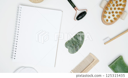 Mock up white notebook, sustainable self-care concept. Eco-friendly beauty products: massage brush, loofah, marble roller, towel, reusable cotton pads 125315435