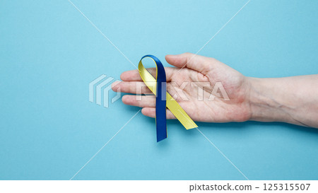 Symbolizing World Down Syndrome Day. A person holds a yellow and blue awareness ribbon Symbolizing World Down Syndrome Day. A person holds a yellow and blue awareness ribbon 125315507