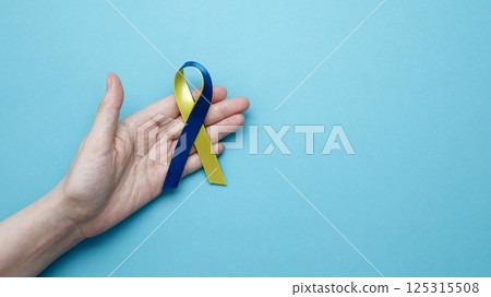 Symbolizing World Down Syndrome Day. A person holds a yellow and blue awareness ribbon 125315508