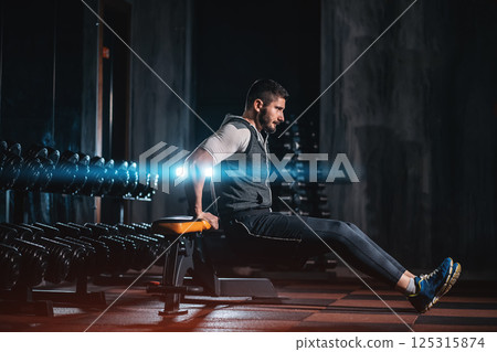 Male bodybuilder performing bench dips for triceps in gym, Man training arm muscles with bench exercise during workout 125315874