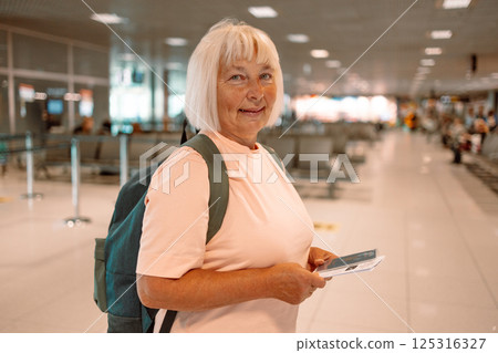 Happy blonde hair Elderly female tourist with a backpack with a passport while waiting for the passport check of the tourist at the airport 125316327