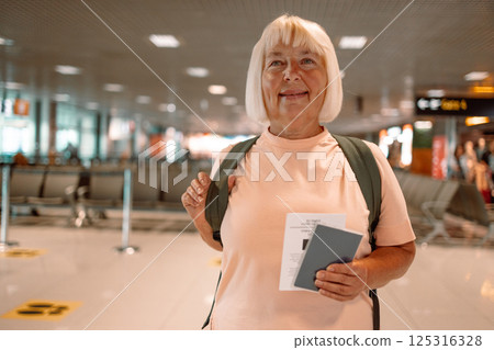 Happy blonde hair Elderly female tourist with a backpack with a passport while waiting for the passport check of the tourist at the airport 125316328