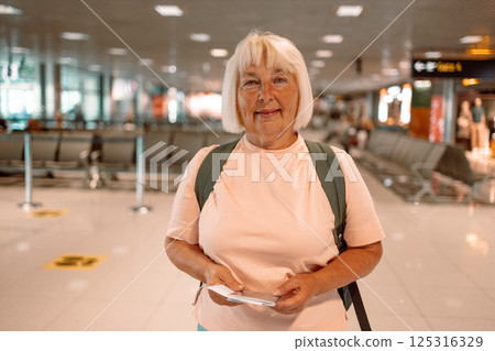 Happy blonde hair Elderly female tourist with a backpack with a passport while waiting for the passport check of the tourist at the airport 125316329