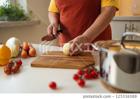 Peeling onion in kitchen for meal preparation. 125316389
