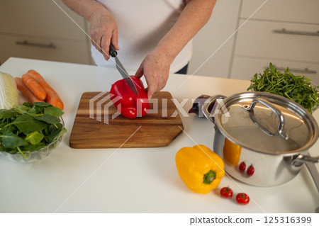 Woman chopping red bell pepper on a wooden cutting board in the kitchen Woman chopping red bell pepper on a wooden cutting board in the kitchen 125316399