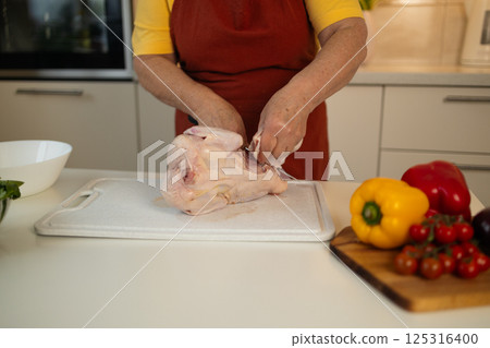 Woman preparing raw chicken in the kitchen for cooking with vegetables 125316400