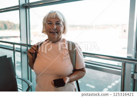 Smiling senior woman at the airport terminal with luggage, ready to travel 125316421