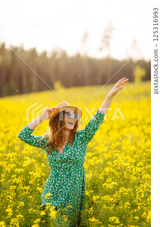 Beautiful woman in bright dress and elegant hat walks and has fun in rapeseed field. Nature, rest. Beautiful woman in bright dress and elegant hat walks and has fun in rapeseed field. Nature, rest. 125316993