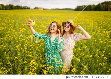 Selfie time.Two Young woman takes selfie while walking flowering field. Nature, relax and lifestyle. 125317205