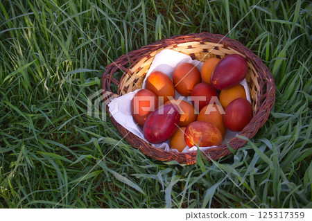 Rustic basket of painted Easter eggs sits nestled in the vibrant green grass. 125317359