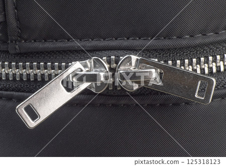 Detailed view shows a metal zipper on black textile surface Detailed view shows a metal zipper on black textile surface 125318123