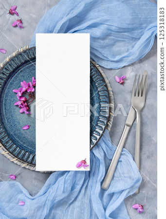 Wedding table place with a card near fabric and wild purple flowers top view on gray, spring mockup 125318183